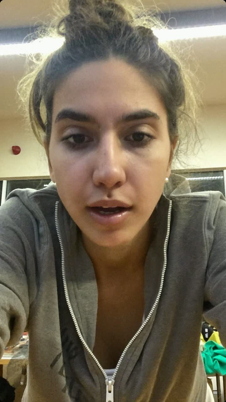 Ayesha, 26-year-old Pakistani woman, messy bun, wearing a grey zip-up and tiny pearl earrings
