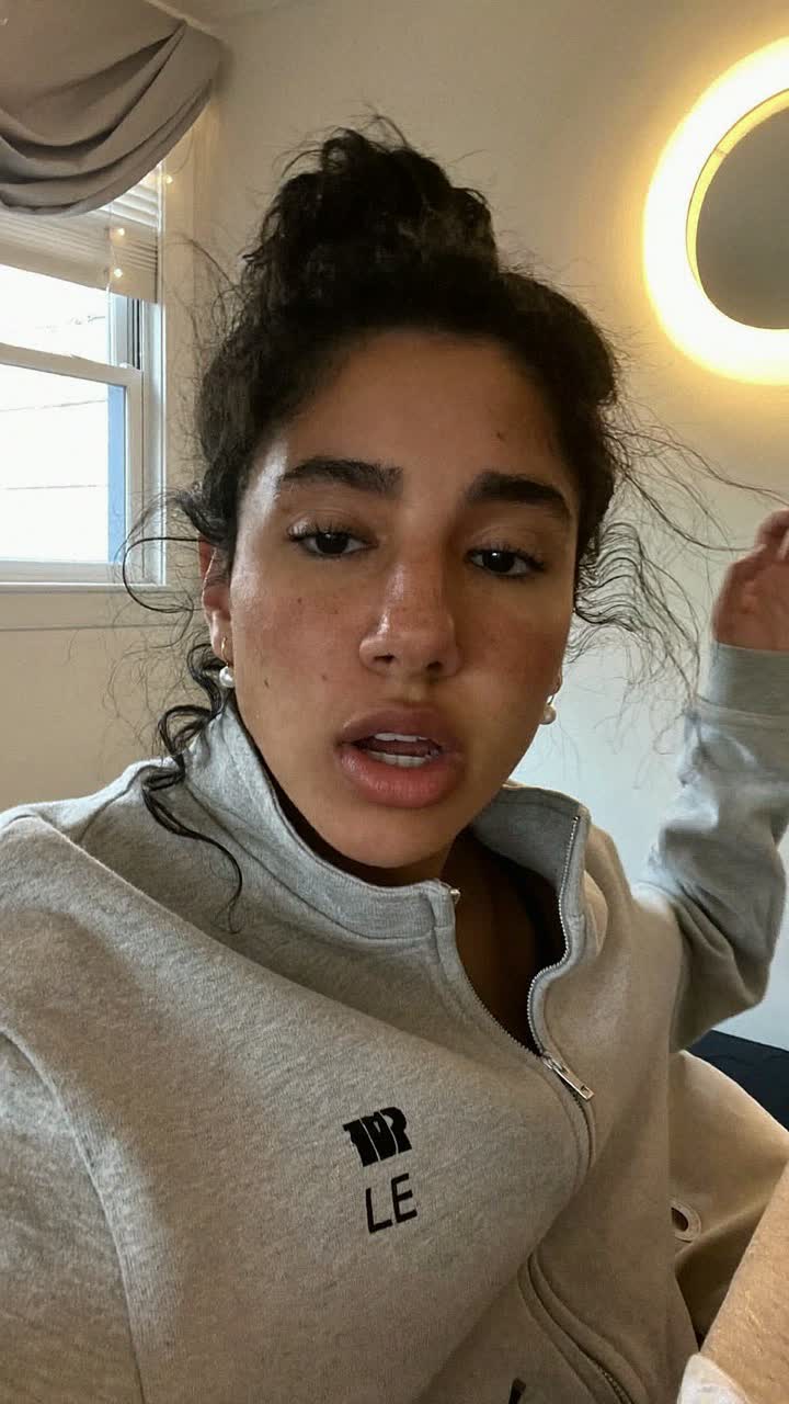 Júlia, 25-year-old Brazilian woman, messy bun, wearing a grey zip-up and tiny pearl earrings