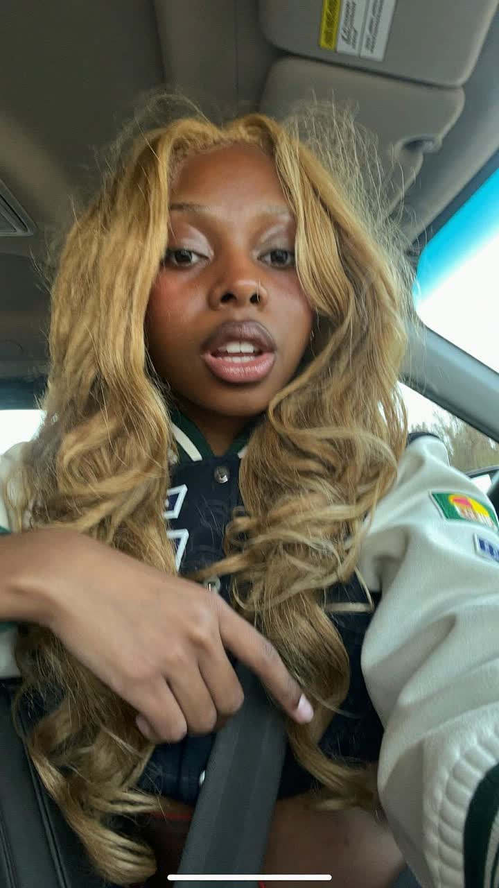 Kayla, 26-year-old Black American woman, honey-blonde waves, wearing a cropped varsity jacket