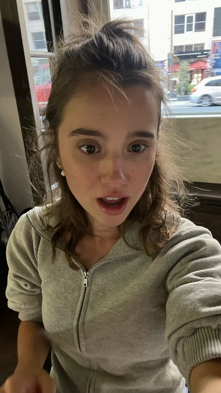 Madison, 33-year-old white American woman, half-up half-down hairstyle, wearing a grey zip-up and tiny pearl earrings
