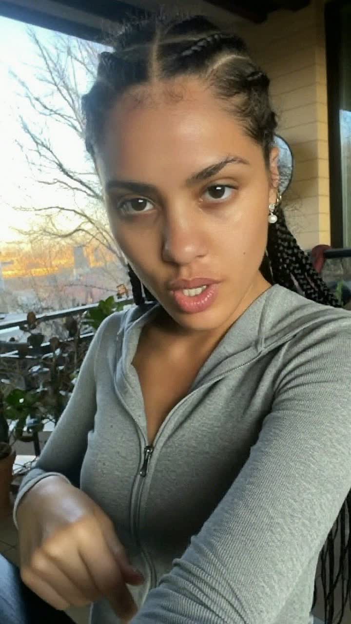 Taylor, 31-year-old white American woman, box braids, wearing a grey zip-up and tiny pearl earrings